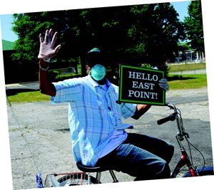 Man on bicycle with "Hello East Point" sign. 